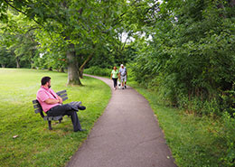 man sitting on bench watching people walk on a trail